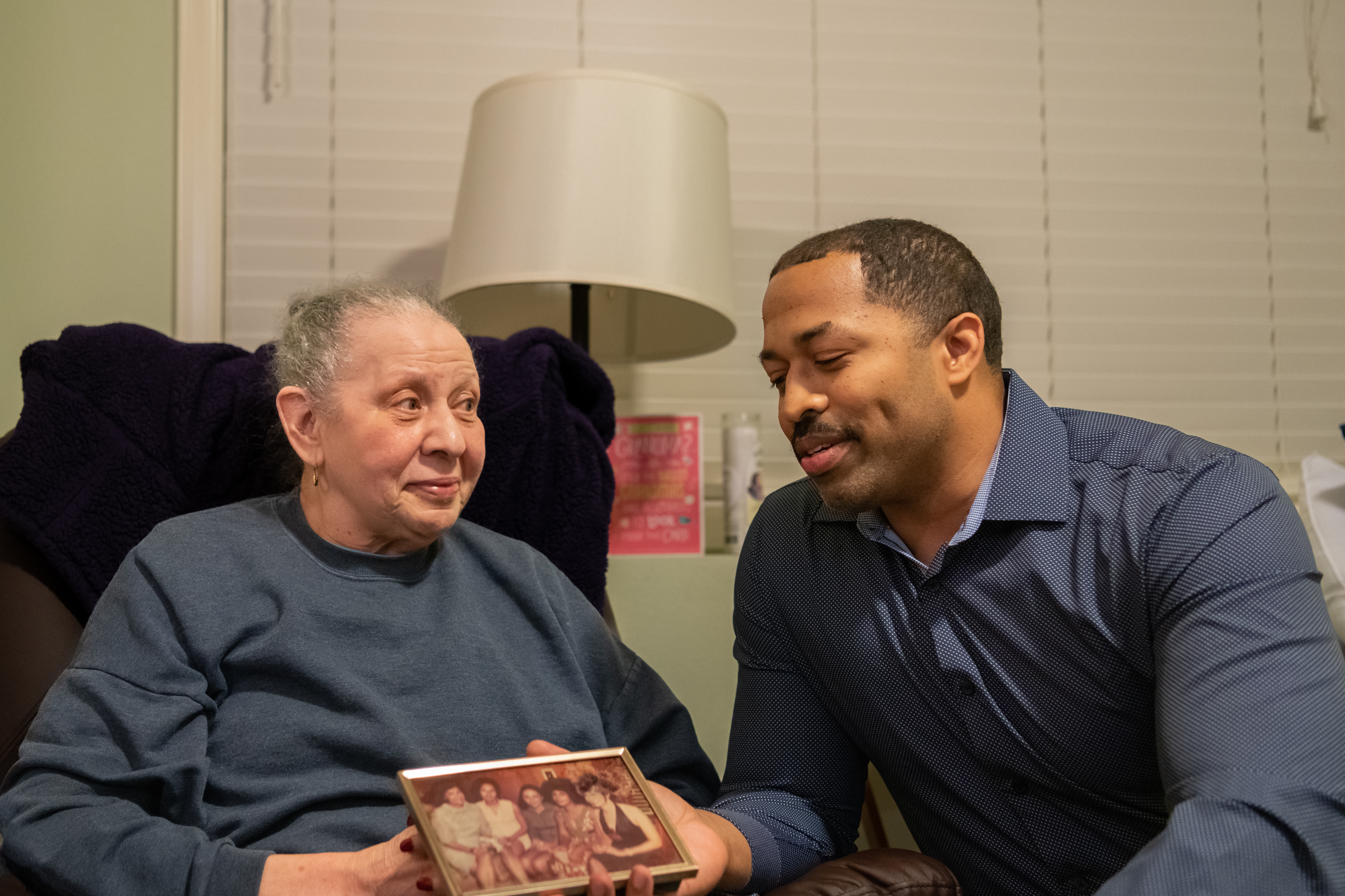 older woman seated next to younger man holding a photo frame 