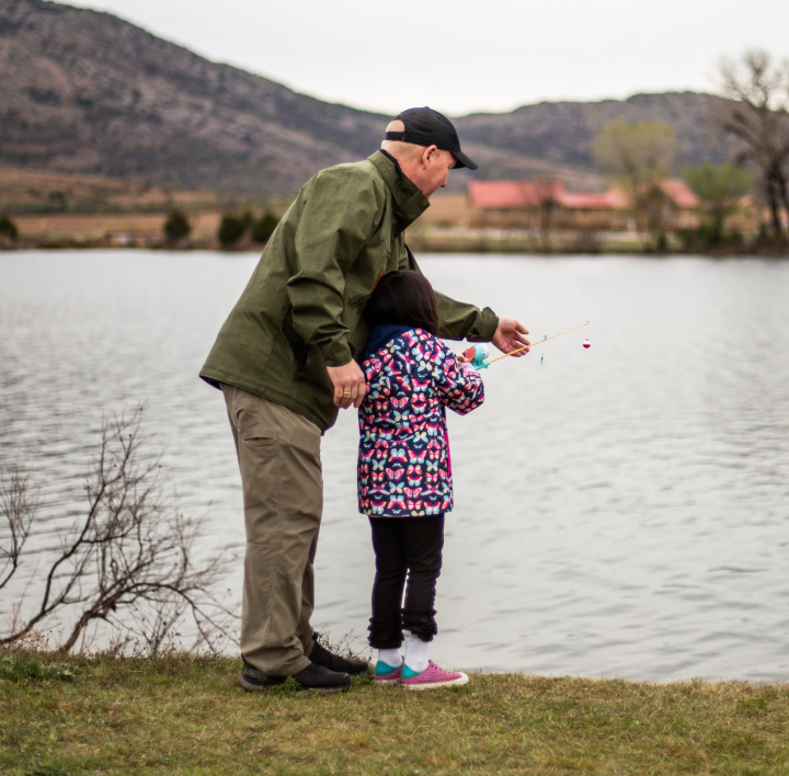 older man standing by the lake fishing with young girl