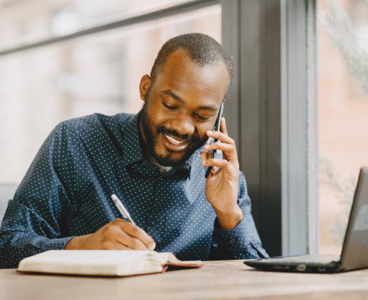 African American man working from home talking on phone and taking notes