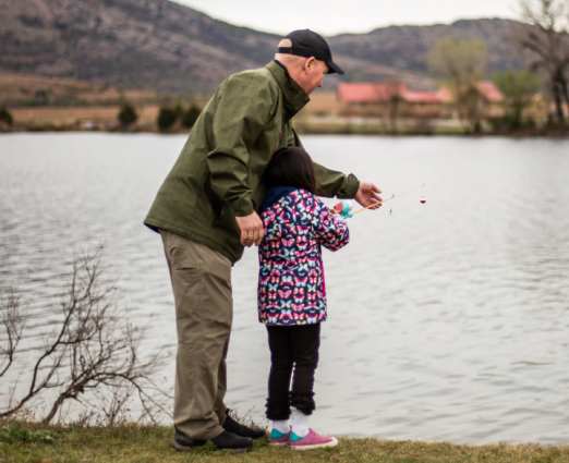 older man standing by the lake fishing with young girl