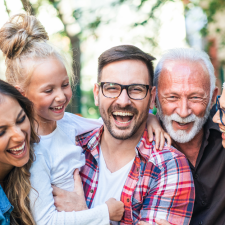 smiling family including grandma, grandpa mother, father, and child close together hugging and smiling