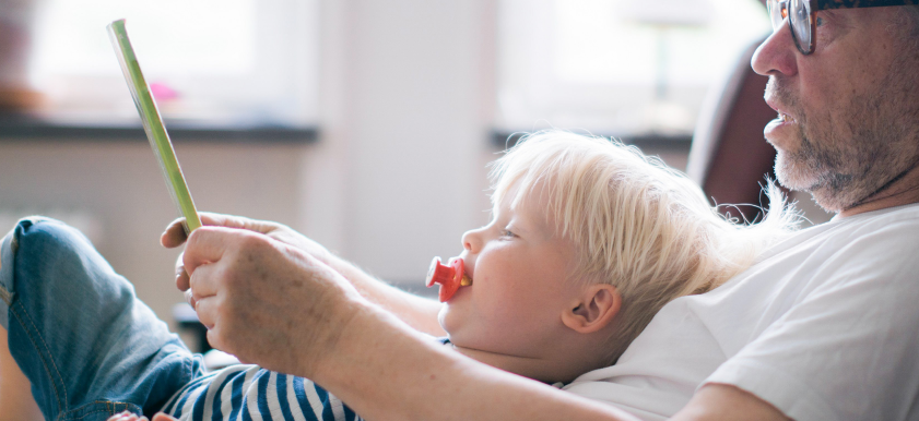 older man reading to toddler on his lap