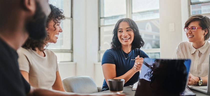 4 office workers sitting around a table looking at a laptop