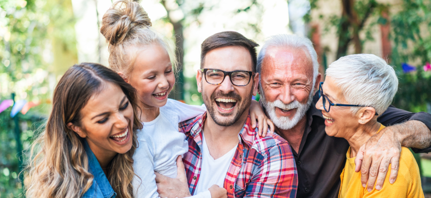 smiling family including grandma, grandpa mother, father, and child close together hugging and smiling