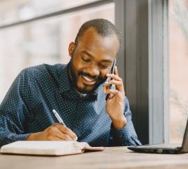 African American man working from home talking on phone and taking notes