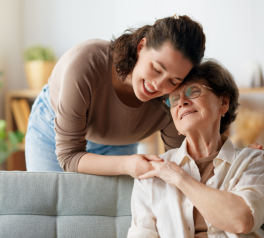 mother and daughter, other sitting on couch daughter standing behind her hugging